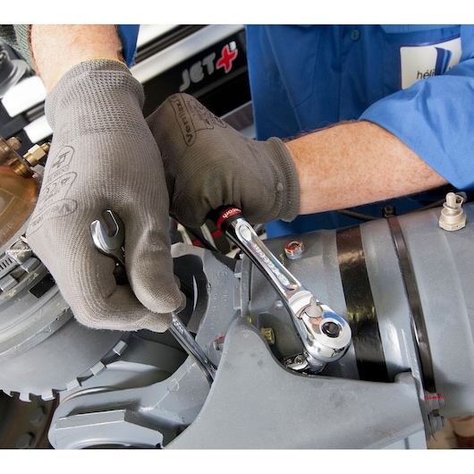 Photo of Facom J.3/4F ratchet wrench in use by mechanic with gloves on machinery.