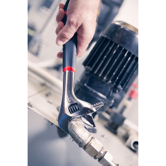 Facom adjustable wrench 101_10GR used to tighten pipe fitting near industrial machinery, close-up.