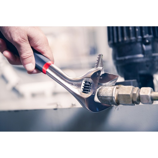 Facom adjustable wrench 101_10GR with black and red handle used to tighten a pipe fitting, close-up photo.