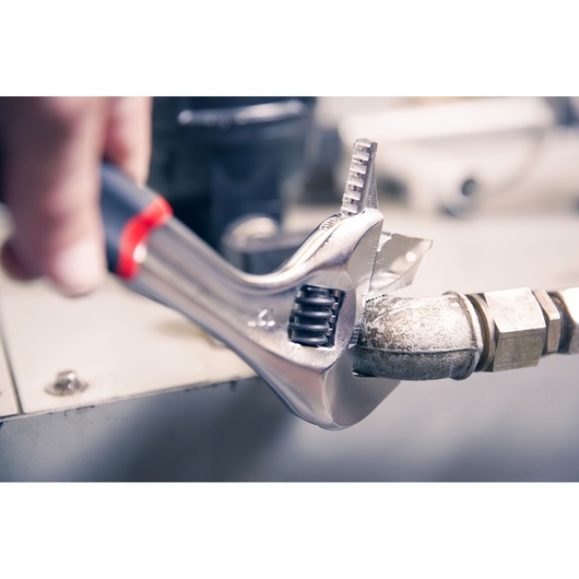 Facom adjustable wrench SKU 101_10GR in use tightening a metal pipe fitting, close-up photography.