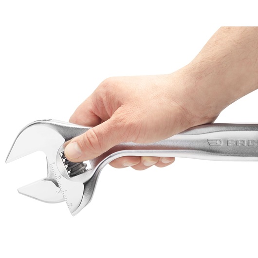Photo of a hand holding a Facom 10110 adjustable wrench, showing the side with logo and adjustment mechanism.