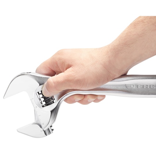 Photo of a hand holding a Facom adjustable wrench 10110, silver finish, close-up on white background.