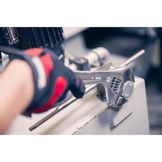 Facom adjustable wrench 101.18PB in use tightening a metal bolt, worker wearing black and red glove.