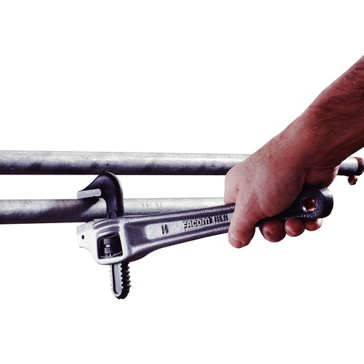 Facom 135A_24 pipe wrench in hand tightening a metal pipe, side angle.