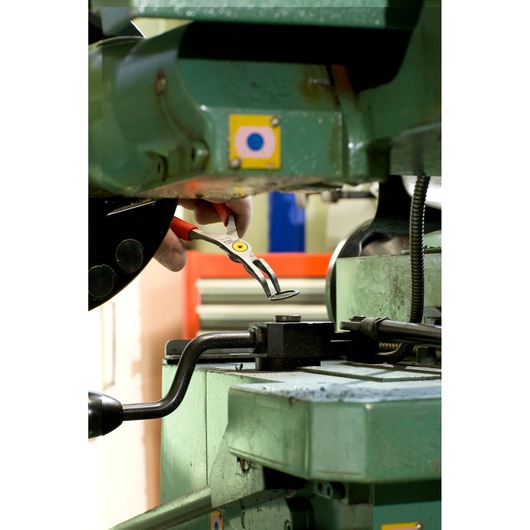 Facom 167A13 pliers with red handles used to grip a metal part on industrial machinery.