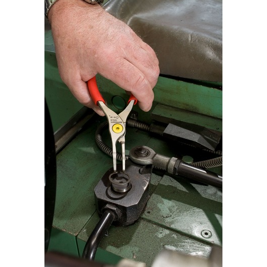 Facom 167A13 circlip pliers with red handles used to remove a circlip in an industrial machine close-up.
