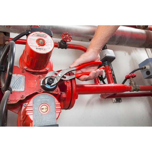 Photo of Facom 170A_25 adjustable pliers being used on red pipe fittings in an industrial setting.