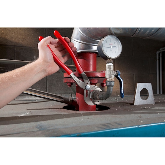 Facom 170A_30 adjustable pliers with red handles used on a pipe valve in an industrial setting.