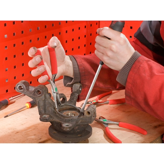 Facom 179A13 pliers with red handles in use on a metal bearing assembly, close-up on workbench.