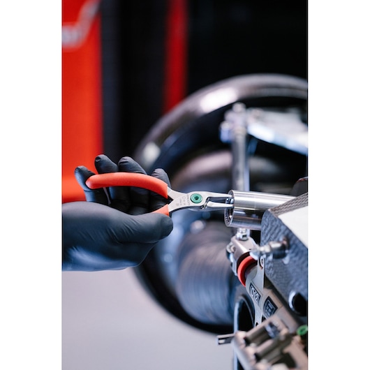 A close-up of a hand wearing a black glove using a Facom tool with red handles to work on mechanical equipment, possibly in an automotive or workshop setting.