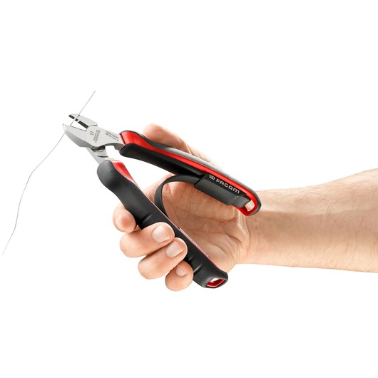 Photo of Facom 192A16CPE diagonal cutting pliers with black and red handles, held in hand cutting wire, side view.