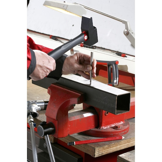 Facom 200C_40 sledge hammer used to strike a punch on a metal beam clamped in a red bench vise, workshop setting.