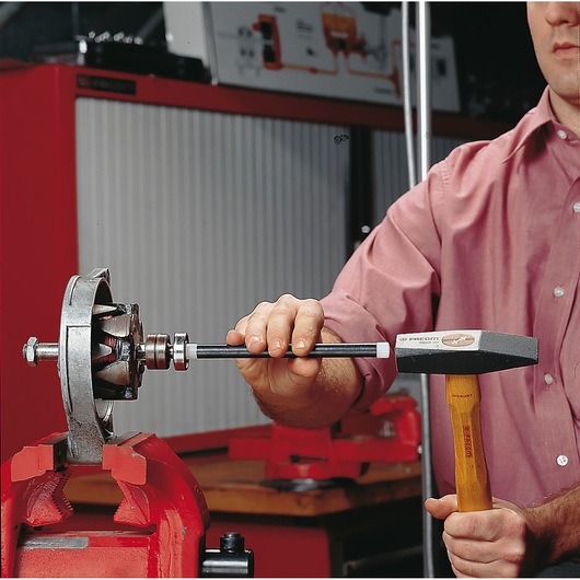 Facom hammer SKU 214_10 used for mechanical assembly on metal part held in red vise, workshop background.