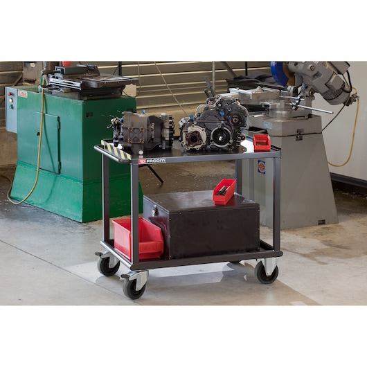 Facom 2702 workshop trolley with metal frame, two shelves, red bins and machinery, shown in industrial setting.