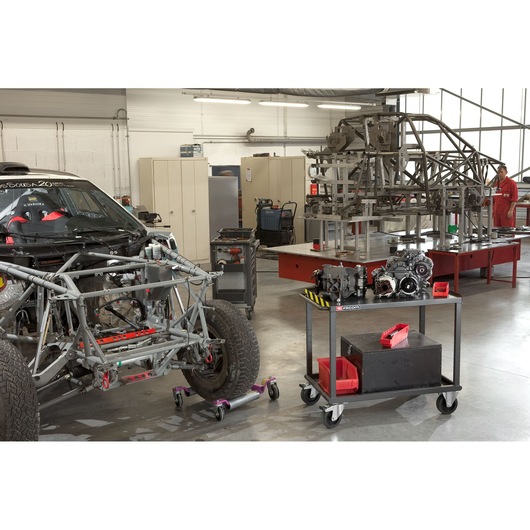 Facom 2702 photography of workshop with race car chassis, metal frame, and tool cart with engine parts.
