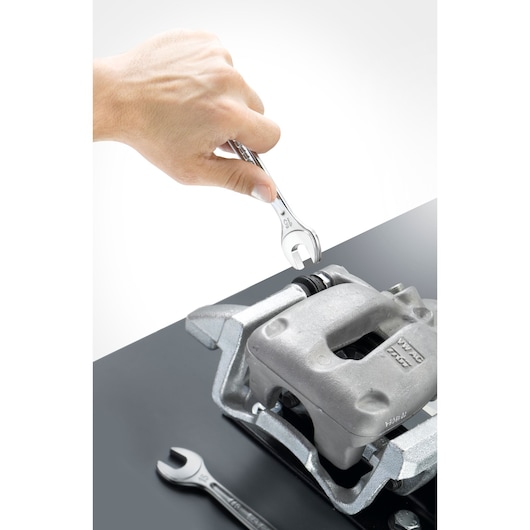 Facom 44030 combination wrench being used on a metal automotive part, close-up angle, another wrench nearby.