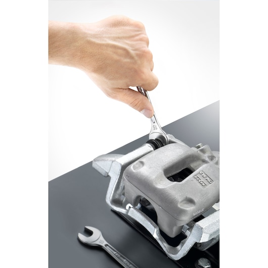 Facom 440_36 photography of hand using wrench on car brake caliper, spanner lying nearby, white background, top angle