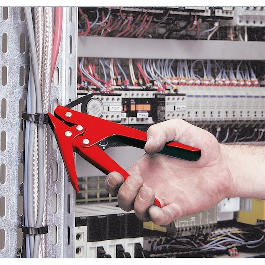 Facom 455B cable tie installation tool in red, used to tighten zip ties on cables in an electrical panel.