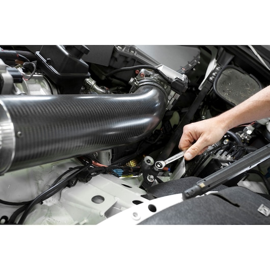 Facom 464TX_10X12 combination wrench used to tighten a bolt in a car engine compartment.