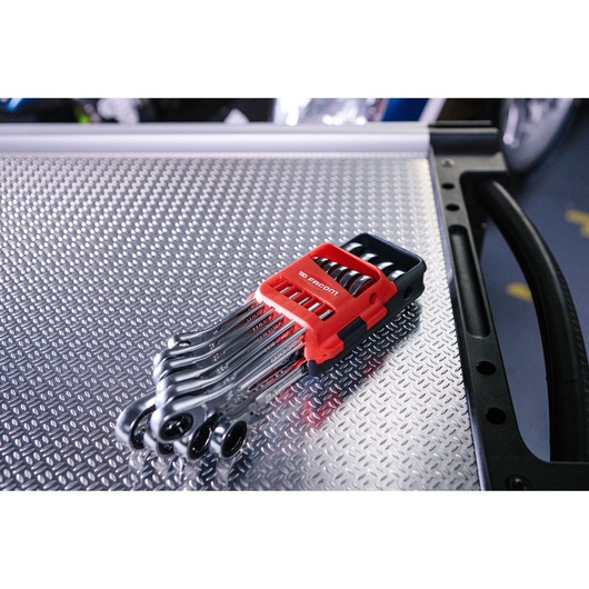 A set of Facom combination ratcheting wrenches in a red and black plastic holder, placed on a textured metal surface.
