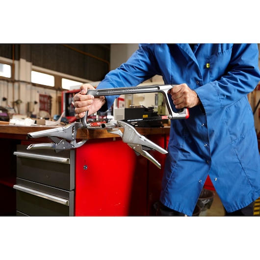 Facom 501A hacksaw held by person in blue coat, clamped to workbench with metal clamps in workshop.