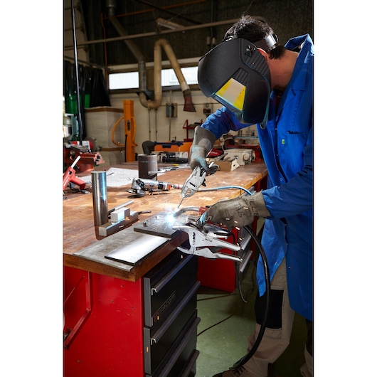 Facom 501A welding clamp in use on a metal workbench during welding operation, workshop setting.