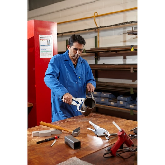 Facom 505A clamp tool used by person in blue lab coat on workshop table with metal parts and tools.