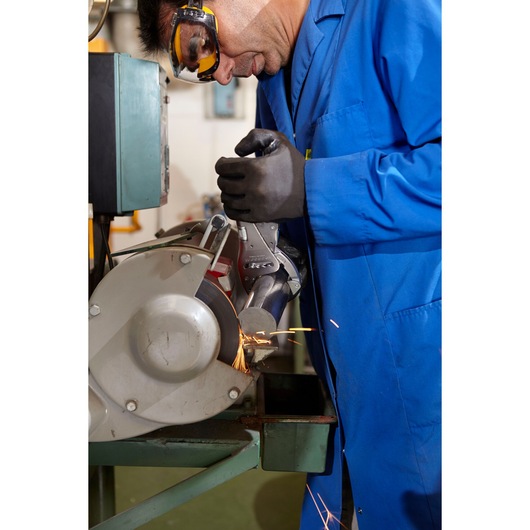 Facom 506A locking pliers clamping a metal pipe on a grinding machine, side view, blue coat and gloves visible.