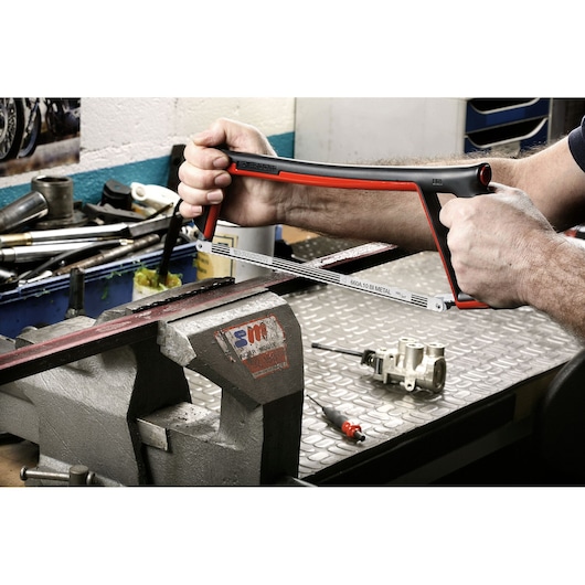 Facom 601 hacksaw with black and red frame, cutting metal in a workshop setting.
