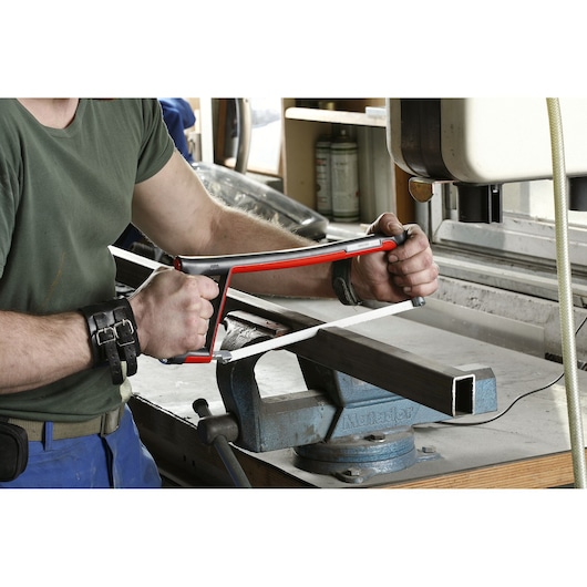Facom 601 hand saw with red frame cutting metal pipe in workshop, close-up of tool in use.