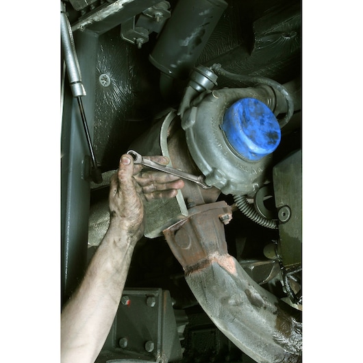 Facom 64_3_4X13_16 photography of a hand using a wrench on a metal automotive part under the vehicle.