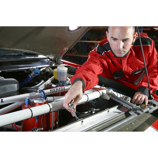 Facom wrench 64_3_4X13_16 in use on a car engine by a person in a red jacket, angled view.