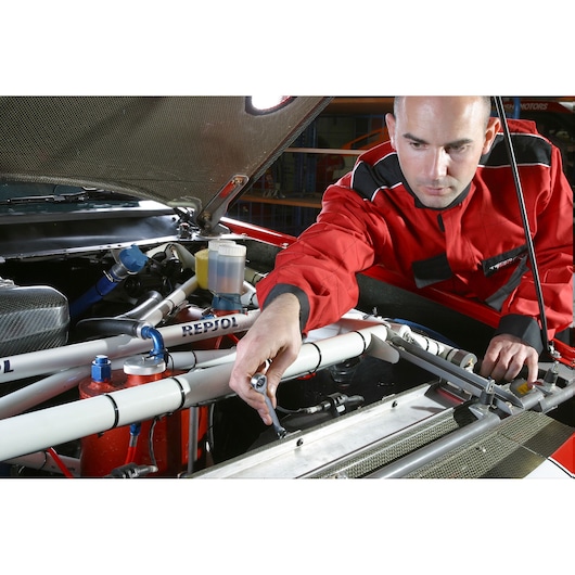 Facom wrench 64_5_8X11_16 used by mechanic in red jacket on car engine, front angle.