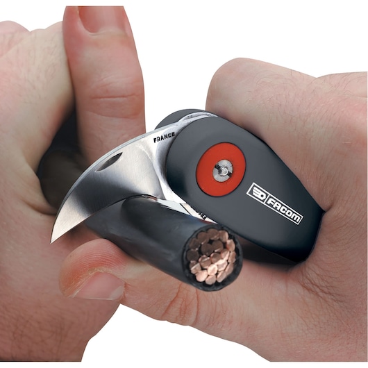 Facom 640180 cable cutter slicing through thick black electrical wire, close-up in hand, blade visible.
