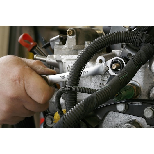 Facom 64C_J2PB ratcheting wrench used on an engine part, mechanic's hand visible, close-up photography.