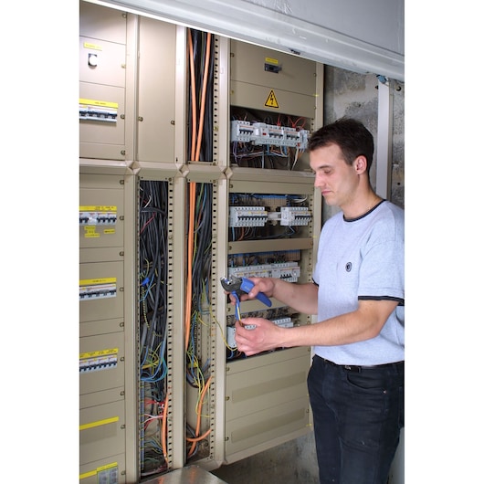 Facom 673838 photography of electrician using pliers at electrical panel with visible wiring.