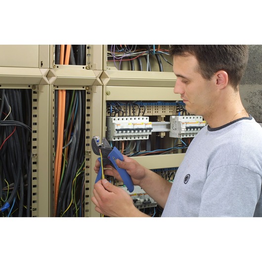 Facom wire stripper 673838 used by technician near electrical panel with cables and terminals.