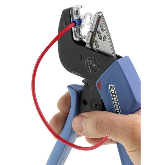 Facom crimping tool 673838 held by hand, blue handles, crimping red wire, close-up with white background.