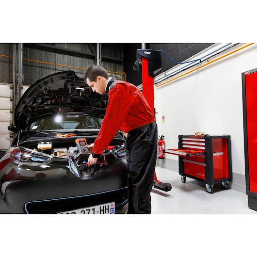 Facom rolling tool cabinet 715PB with open drawer in garage next to mechanic working on car.