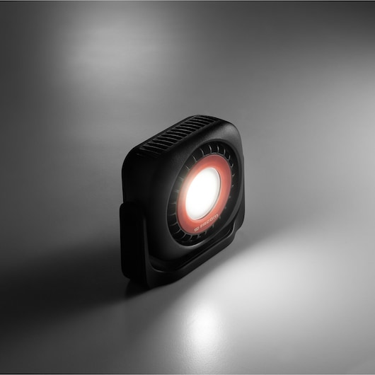 Facom 779.1000BLPB compact LED work light with black housing and red trim, angled left, illuminating surface.