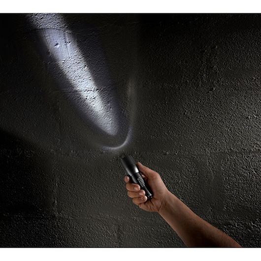 Photo of a hand holding a Facom 779_CBT black flashlight shining a bright beam onto a dark textured wall.