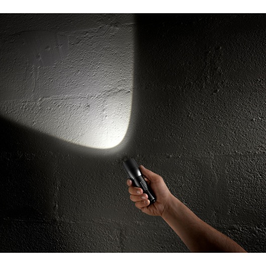 Photo of a hand holding a Facom 779_CBT flashlight shining a bright beam on a dark textured wall.