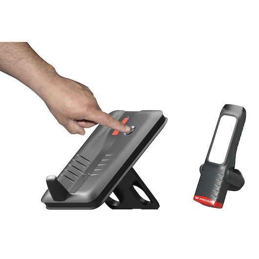 Facom 779.CL5PB rechargeable LED work light and charging base, close-up of hand pressing power button, side view.