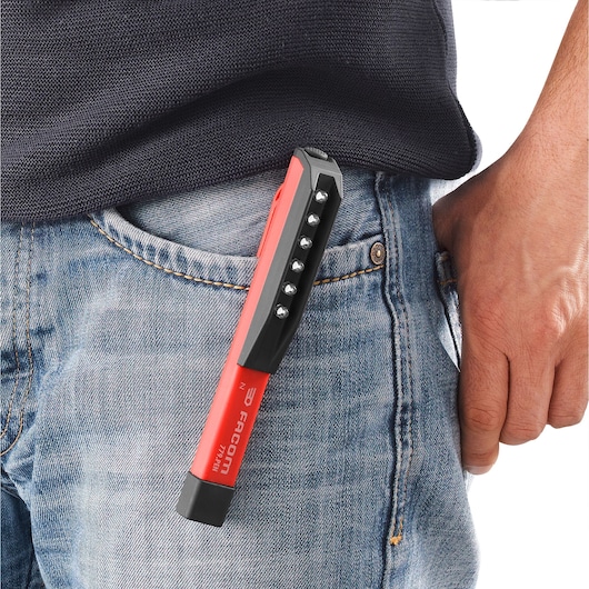 A red Facom penlight, model 779.PENPB, clipped onto the front pocket of blue jeans worn by a person. The penlight features multiple LED lights arranged in a line.