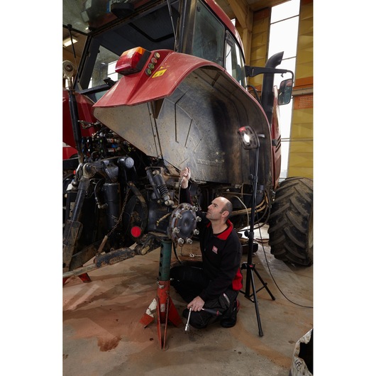 Photo of Facom 779_TRIPOD photography tripod used for work lighting, positioned near a mechanic repairing a red tractor.