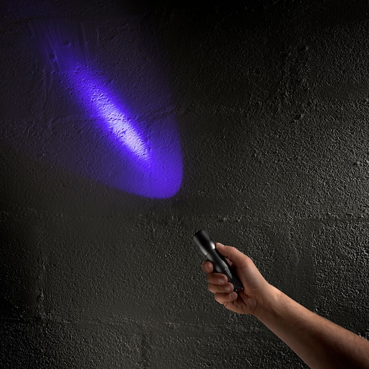Facom 779UVT UV flashlight in hand shining purple light on dark wall, angled view.