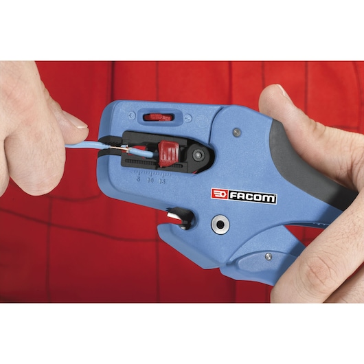Facom 793936 precision wire stripper tool held in hand, blue body, stripping blue wire, close-up.