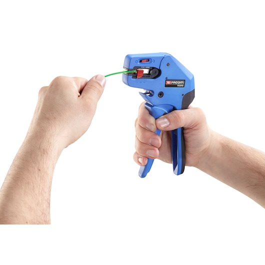 Facom 793940 wire stripper tool held in hand, blue color, in use stripping green wire, front angle.