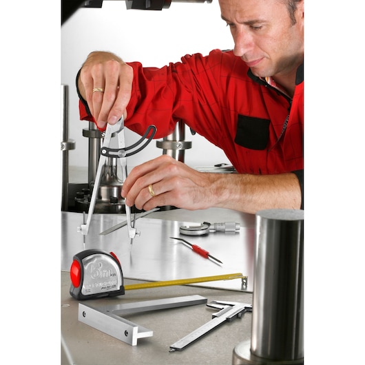 Facom measurement tools 823_25 on workbench with person in red shirt using calipers, tape, and ruler visible.