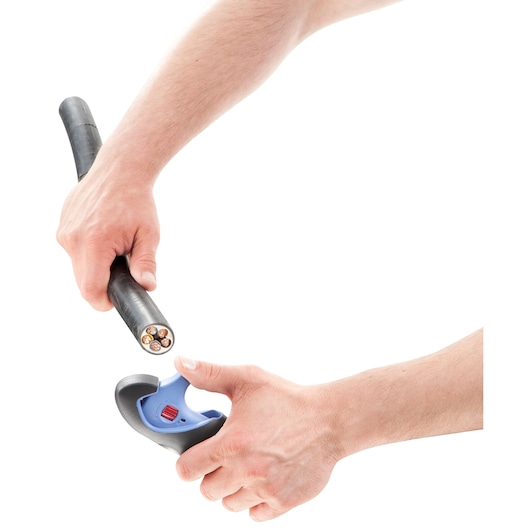 Two hands using a Facom cable stripper tool to strip insulation from a thick electrical cable, showing copper wires inside.